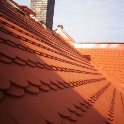 MP-BUD Usługi Budowlane - Nowy dach pokryty dachówką karpiówką w odcieniach czerwieni, z widocznym kominem z cegły i fragmentem nieba z lekkimi chmurami.