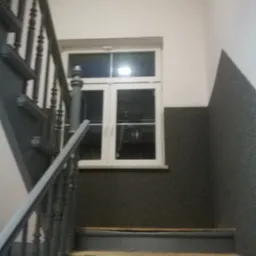 Klatka schodowa w Nowej Soli z oknem na półpiętrze, ściany częściowo pokryte szarym, chropowatym tynkiem.