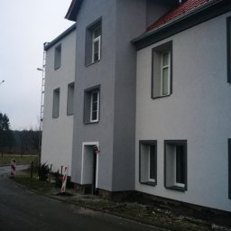 MP-BUD Usługi Budowlane - Dwukondygnacyjny budynek po ociepleniu i pomalowaniu elewacji na odcienie szarości, z czerwoną dachówką, widok z poziomu ulicy w pochmurny dzień.