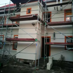 Budynek wielorodzinny w Nowej Soli w trakcie prac elewacyjnych, widoczne rusztowania, świeżo pomalowana fasada w kolorze kremowym z pomarańczowymi obramowaniami okien i drzwi.