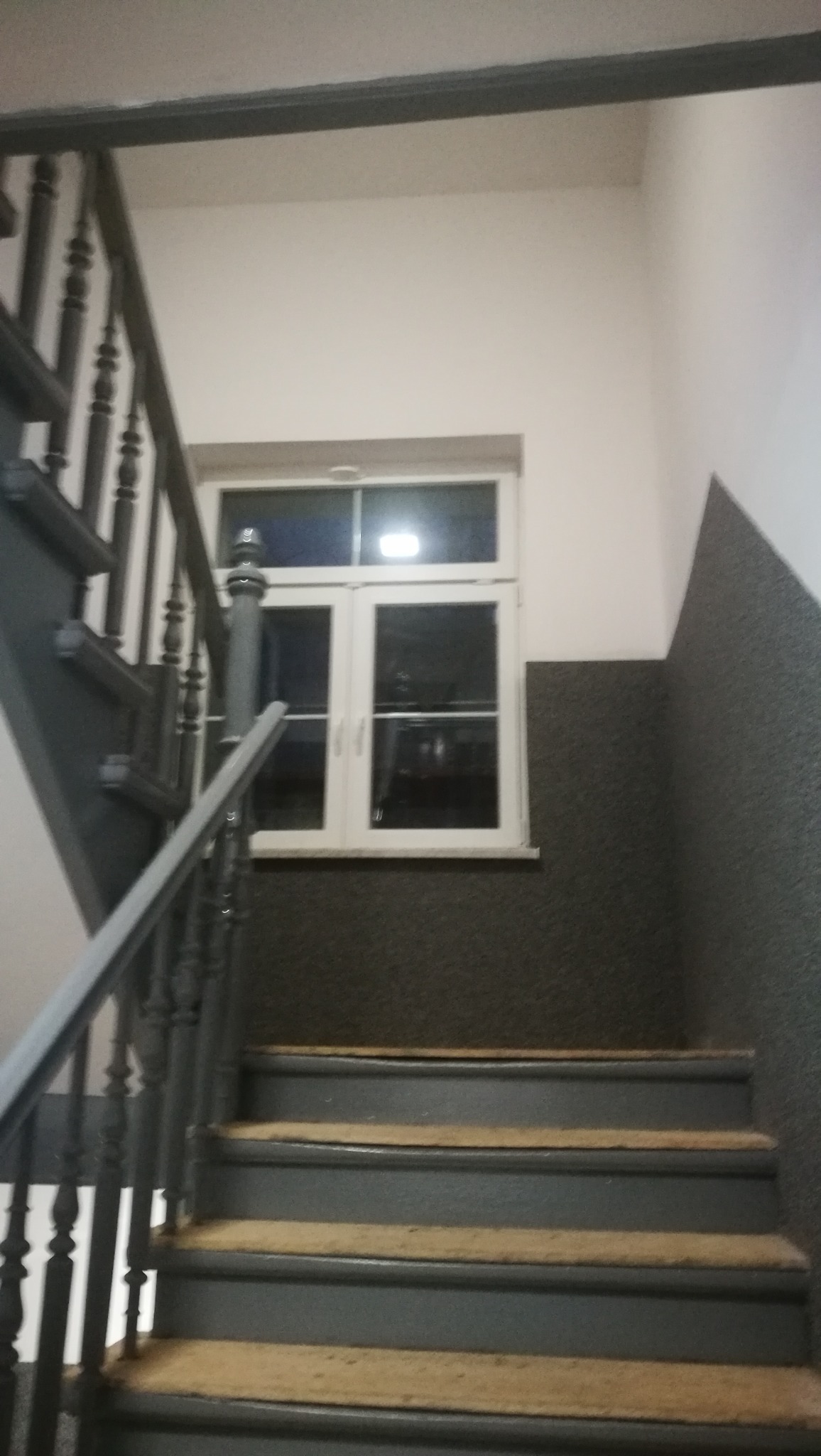 Klatka schodowa w Nowej Soli z oknem na półpiętrze, ściany częściowo pokryte szarym, chropowatym tynkiem.