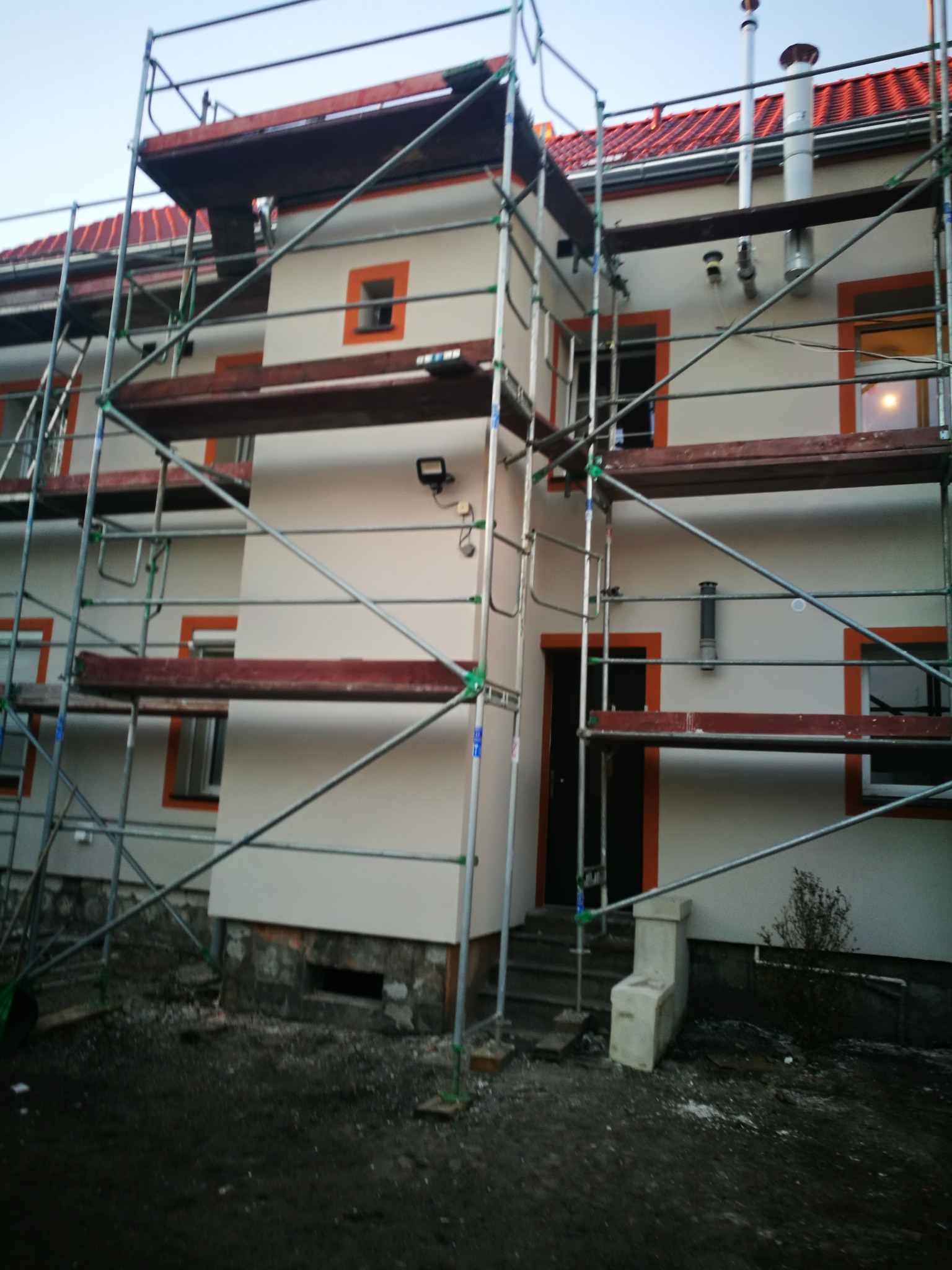 Budynek wielorodzinny w Nowej Soli w trakcie prac elewacyjnych, widoczne rusztowania, świeżo pomalowana fasada w kolorze kremowym z pomarańczowymi obramowaniami okien i drzwi.