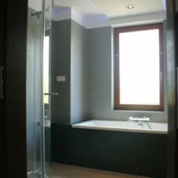 Nowoczesna łazienka z kabiną prysznicową z zaokrąglonym szkłem, podświetlanym sufitem i oknem z drewnianą ramą nad wanną.