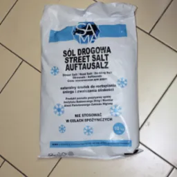 Worek 10 kg soli drogowej, leżący na jasnych płytkach podłogowych, z widocznym logo SAMA i napisem 'Sól Drogowa Street Salt Auftausalz'.