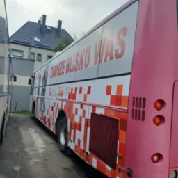 Różowy autobus z reklamą radiową i wzorem w kratę, zaparkowany na zewnątrz budynku.