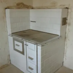 Biały, kaflowy piec kuchenny z metalowymi detalami, w rogu pomieszczenia z surowymi ścianami. Widoczne drzwiczki i szuflady.