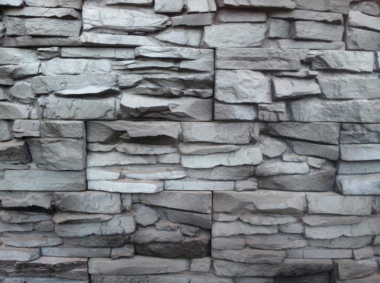 Ściana wyłożona szarym kamieniem ozdobnym o nieregularnych kształtach i fakturze, imitującym naturalny skarn.