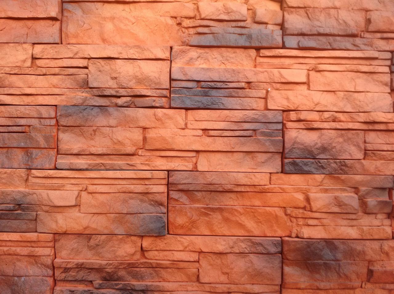 Pomarańczowo-szare płytki elewacyjne imitujące kamień naturalny, ułożone w nieregularny wzór.