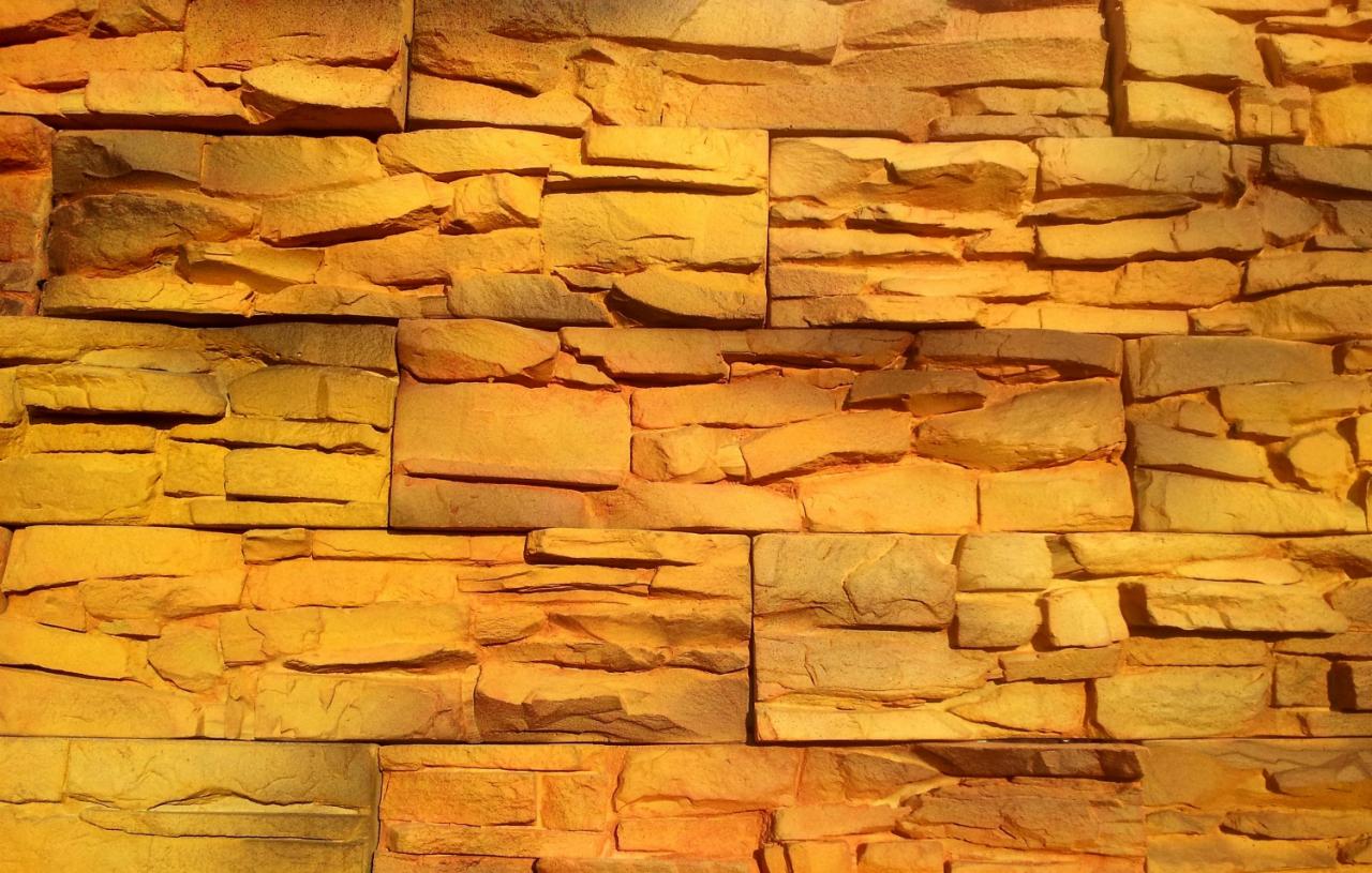 Ściana wyłożona dekoracyjnym kamieniem w odcieniach złota i brązu, imitującym naturalny skarn, z wyraźną fakturą i nieregularnym kształtem poszczególnych elementów.