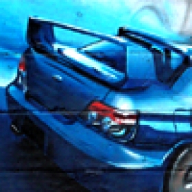 Niebieski samochód sportowy z dużym spojlerem, namalowany jako graffiti na ścianie. Ujęcie z tyłu, widoczne światła i fragment koła. Dominują odcienie niebieskiego i szarości.