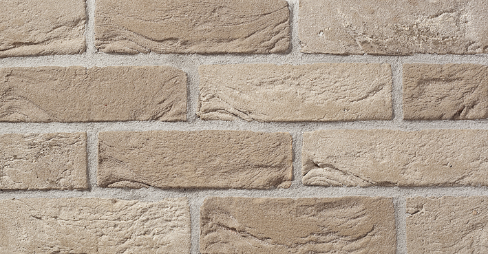 Fragment ściany z dekoracyjnej, ręcznie formowanej cegły w odcieniach beżu i brązu z wyraźną fakturą i jasną fugą.