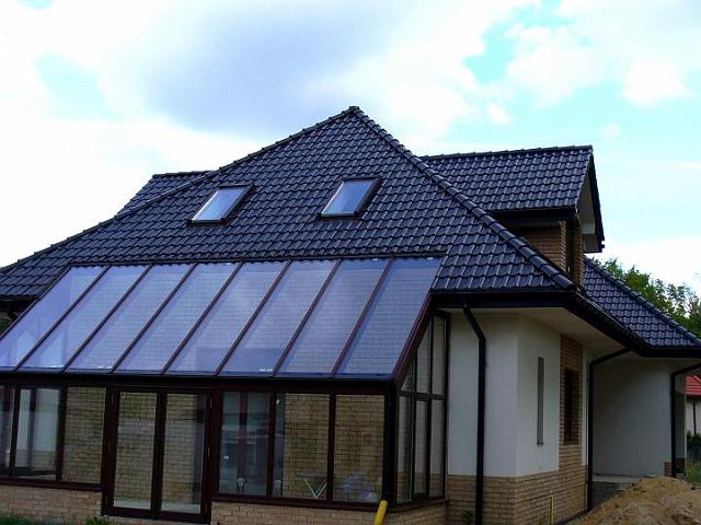 Dom jednorodzinny z ciemną dachówką ceramiczną i oknami dachowymi, dobudowana przeszklona weranda z ceglaną podstawą.