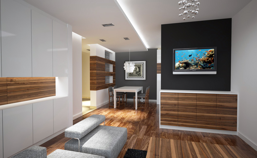 Nowoczesne wnętrze mieszkania z drewnianą podłogą, szarą sofą modułową, białymi szafkami i ścianą z telewizorem wyświetlającym rafę koralową.