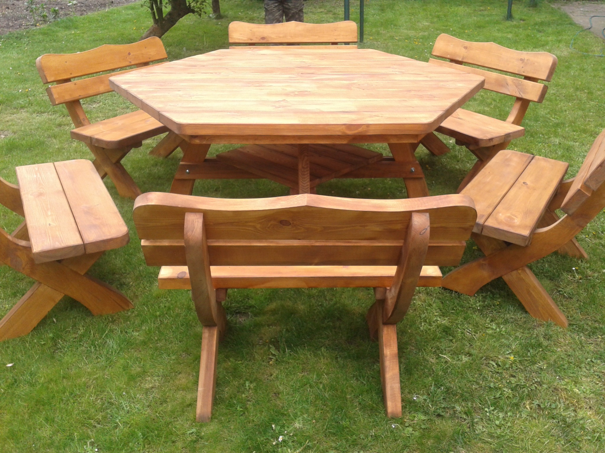 Zestaw ogrodowy: heksagonalny stół i sześć krzeseł z jasnego drewna na trawniku.