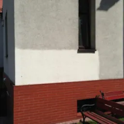 Fragment ściany budynku w Katowicach po częściowym oczyszczeniu, widoczna różnica w kolorze elewacji, ceglana podmurówka i fragment ławki.