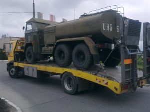 Żółta laweta przewozi wojskowy pojazd cysternę w kolorze khaki z napisem UHO 5.