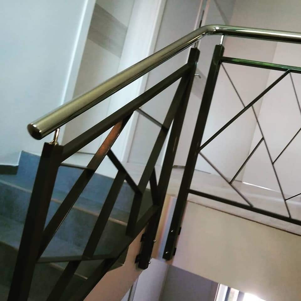 Metalowa balustrada schodowa z geometrycznym wypełnieniem, polerowana poręcz, widok z dołu, szare stopnie schodów.