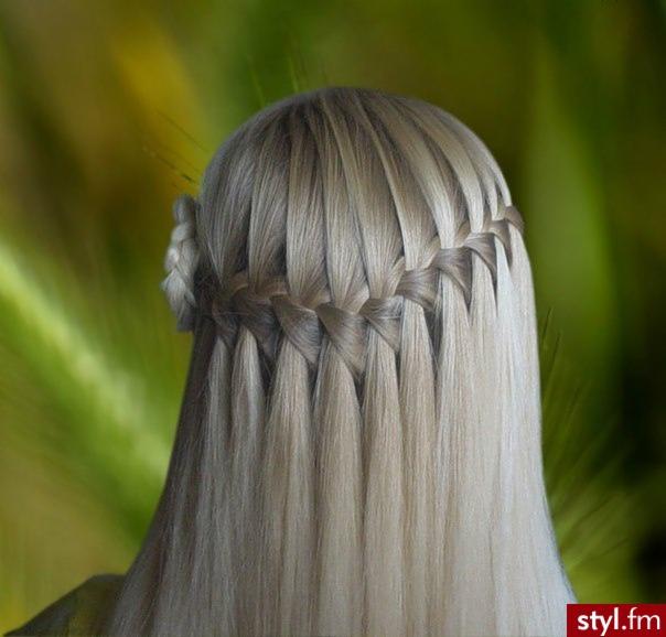 Tył głowy z blond włosami upiętymi w warkocz wodospad z ozdobnym kwiatkiem po lewej stronie, na rozmytym zielono-żółtym tle.