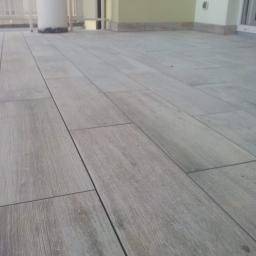 Prywatna osoba - Ułożona szara, prostokątna terakota imitująca drewno na balkonie, widok z niskiej perspektywy, jasne światło.