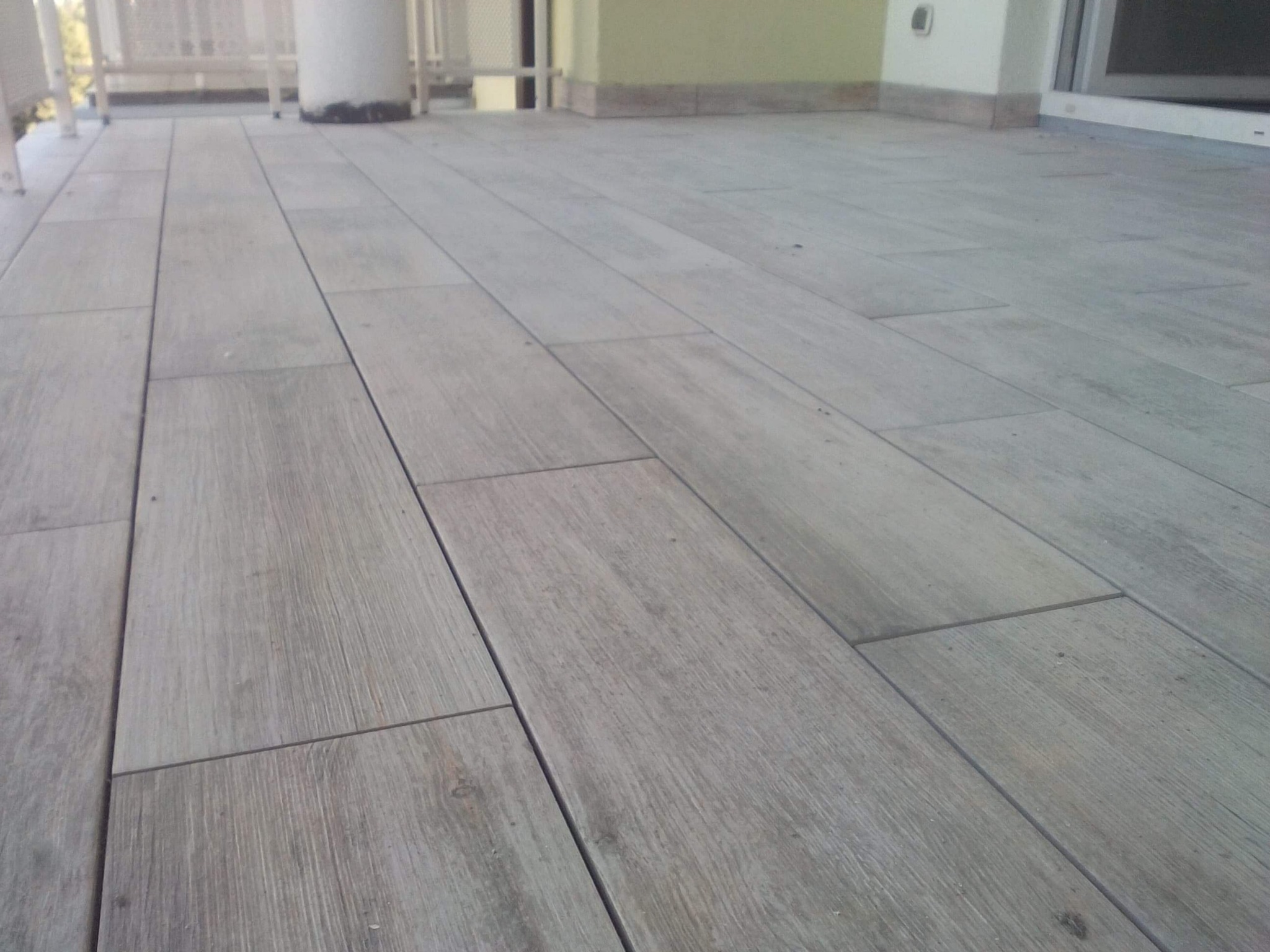 Ułożona szara, prostokątna terakota imitująca drewno na balkonie, widok z niskiej perspektywy, jasne światło.