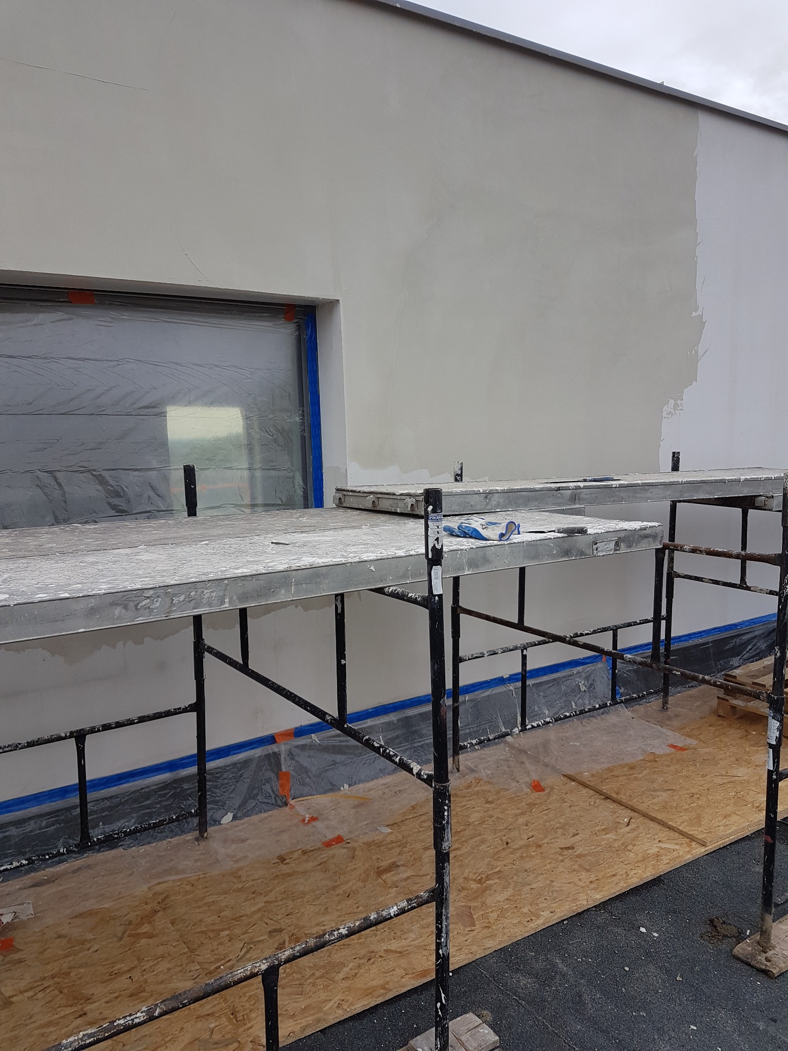 Elewacja budynku w trakcie prac w Gorzowie Wielkopolskim, widoczne rusztowanie, zabezpieczone okno folią i fragment pomalowanej ściany.