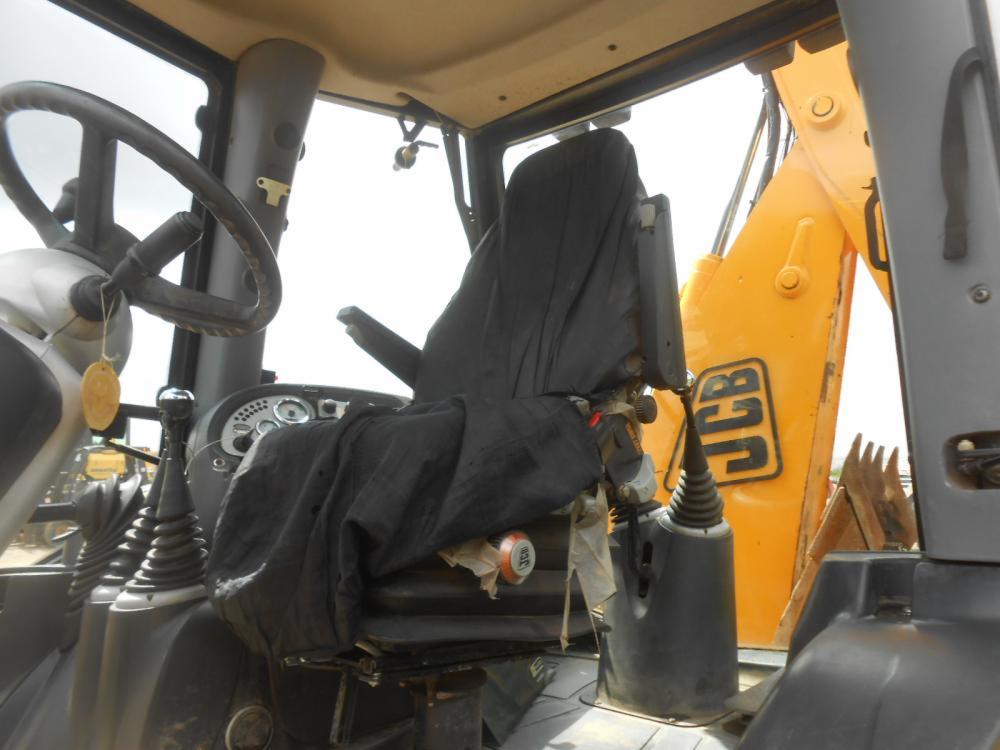 Wnętrze kabiny koparko-ładowarki JCB z Dobra, z czarnym pokrowcem na siedzeniu i widocznym żółtym ramieniem koparki.