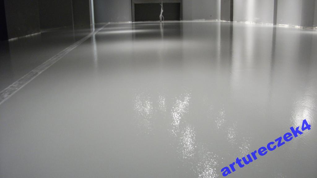 Jasnoszara posadzka epoksydowa z delikatnym połyskiem, widoczne łączenia i refleksy świetlne, minimalistyczne wnętrze.