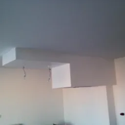 Wnętrze pokoju z pomalowanymi ścianami na biało, widoczna sufitowa konstrukcja z wystającymi przewodami elektrycznymi bez opraw oświetleniowych.