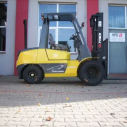 Żółty wózek widłowy GC.POWER FG/FD 35 z czarnym napisem Silver Leopard na tle szarego budynku z czerwonymi akcentami, liście na brukowanej nawierzchni.