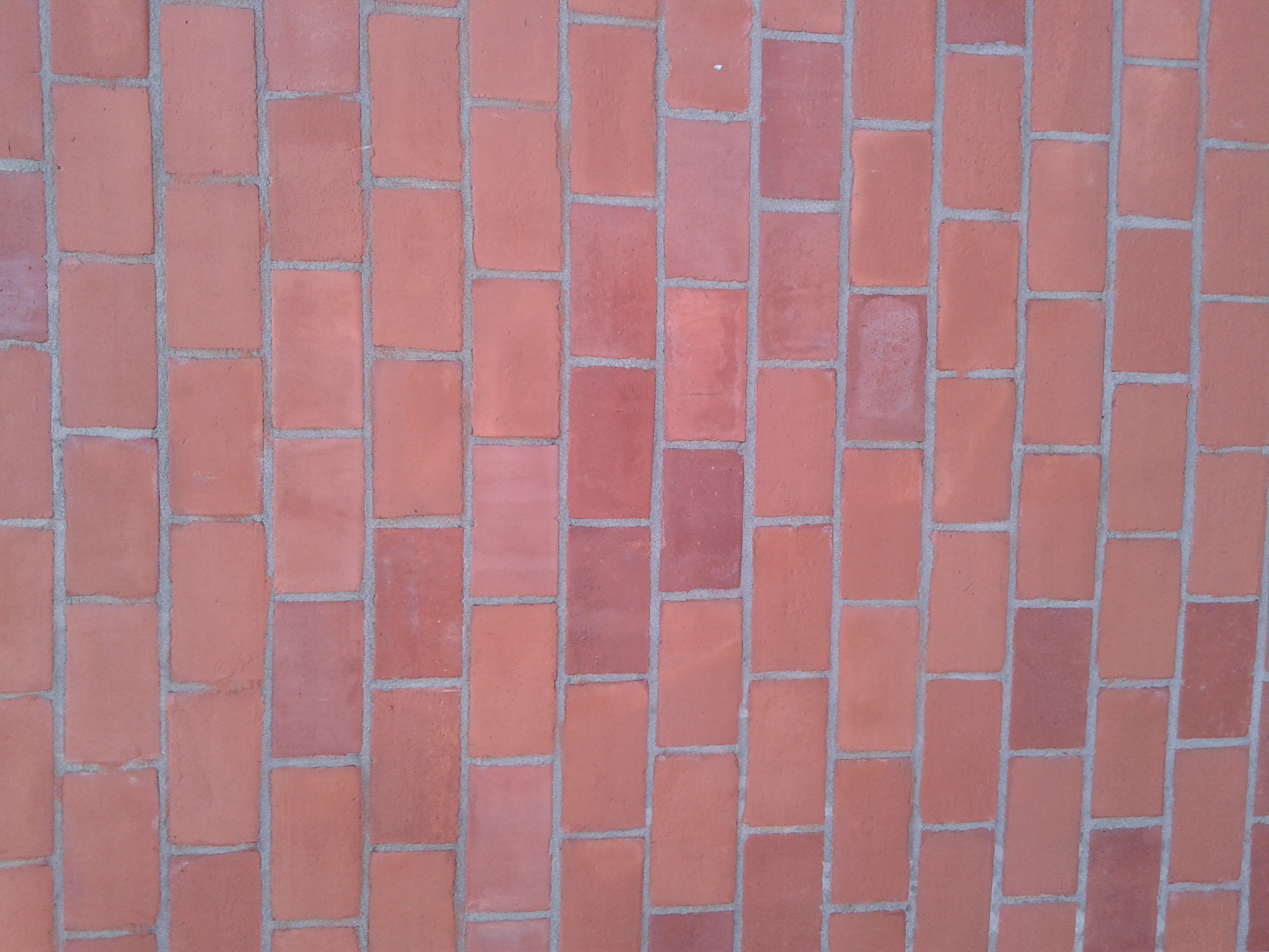 Czerwona ceglana posadzka ułożona w regularny wzór z szarymi fugami. Ujęcie z góry, prezentujące detal wykończenia podłoża.