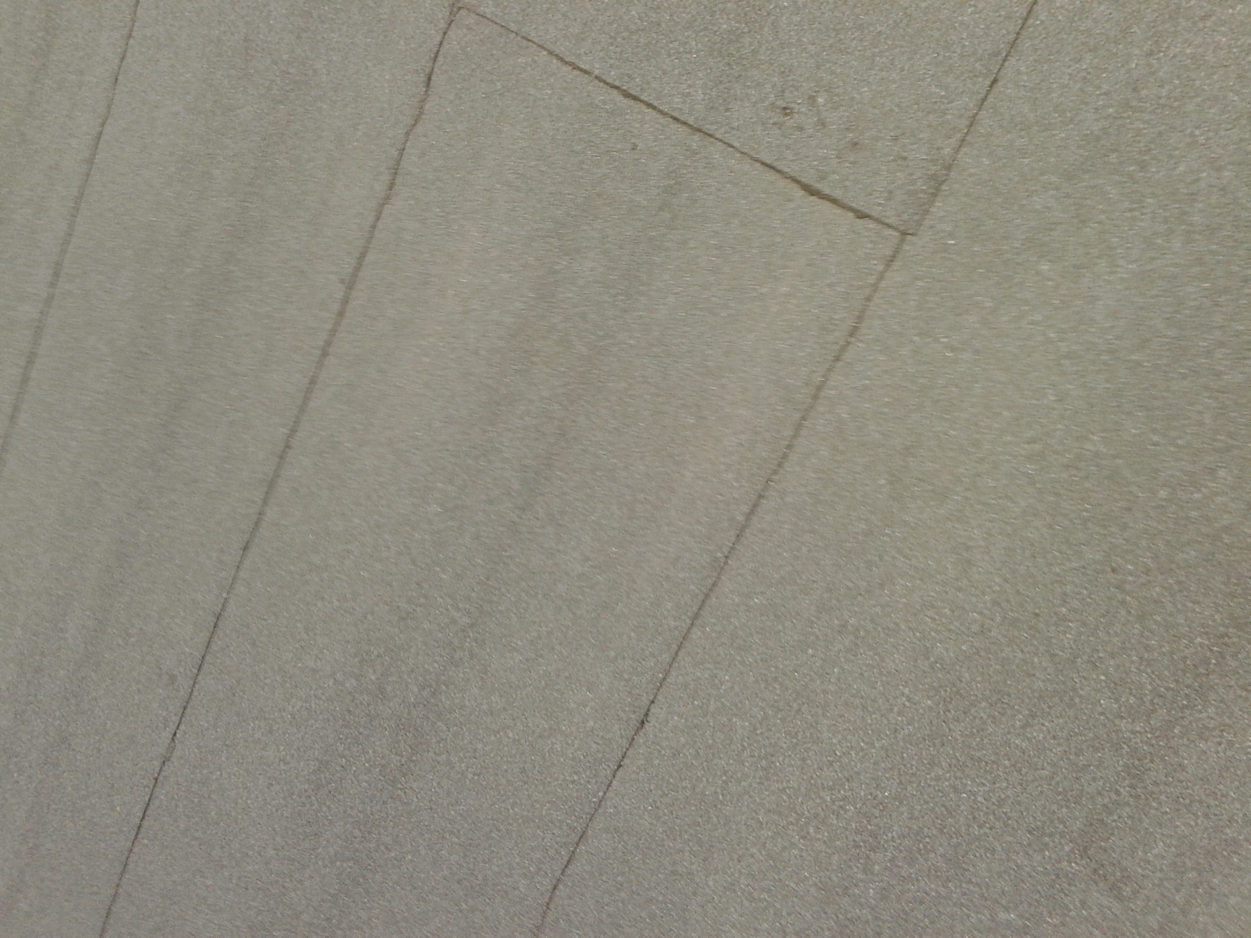 Jasnoszara, ukośna powierzchnia z widocznymi spoinami między płytami, przypominająca kamienny taras lub schody. Powierzchnia ma delikatną fakturę.