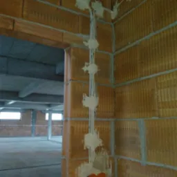 Montaż przewod&oacute;w elektrycznych w nowym budynku z cegły, kable zabezpieczone gipsem, widoczne pomarańczowe rury instalacyjne w ścianie.