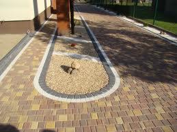 Ułożona z kostki brukowej ścieżka z ozdobnym obramowaniem i wypełnieniem z drobnego żwiru, prowadząca wzdłuż budynku.