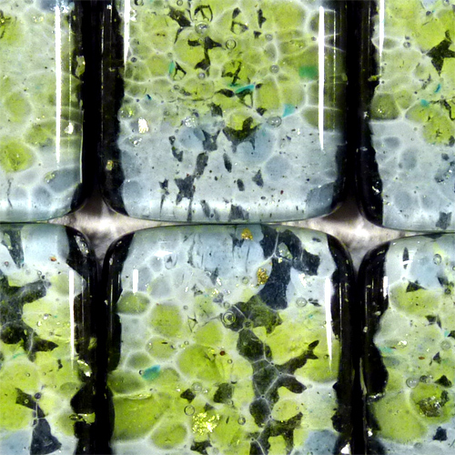 Zbliżenie na dekoracyjne, szklane płytki w odcieniach zieleni, szarości i czerni z zatopionymi drobinkami złota, tworzące mozaikę.