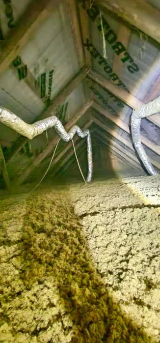 Ocieplenie poddasza wełną mineralną z widocznymi przewodami wentylacyjnymi. Widok z dołu na skośny dach z drewnianą konstrukcją i izolacją.