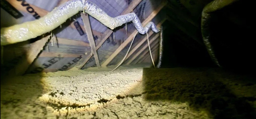 Ocieplenie poddasza wełną mineralną, widoczne krokwie i przewody wentylacyjne. Oświetlenie punktowe podkreśla strukturę materiału izolacyjnego.