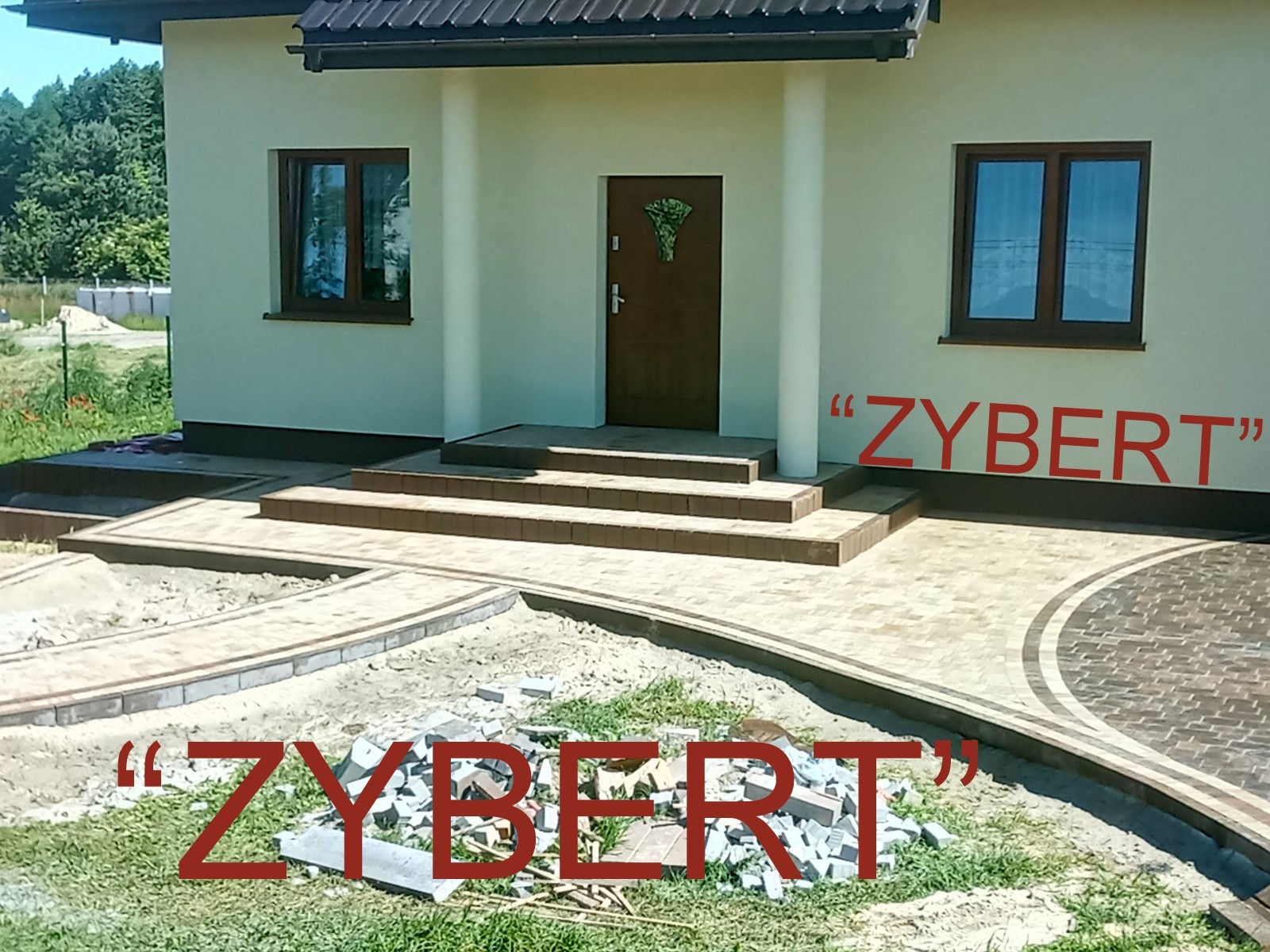 Nowo wyłożony chodnik z kostki brukowej przed domem, z widocznym fragmentem niezakończonej pracy i stertą kostki na trawniku.