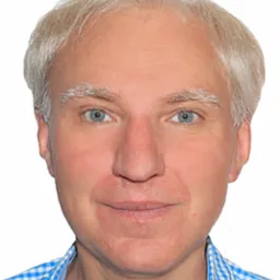 Portret mężczyzny z siwymi włosami i niebieskimi oczami, ubranego w niebiesko-białą koszulę w kratę, na białym tle.