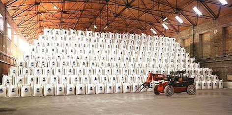 Magazyn soli drogowej w workach Big-Bag ułożonych piramidalnie, transportowanych przez wózek widłowy Manitou, widok na konstrukcję dachu magazynu.