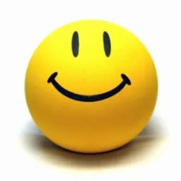 Żółta piłeczka z narysowaną czarną, uśmiechniętą buźką, leżąca na białym tle.