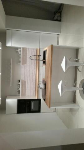 Nowoczesna, minimalistyczna kuchnia z białymi szafkami, drewnianym blatem i białymi stołkami barowymi, widziana z perspektywy lekko z góry.