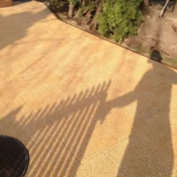 Ułożona, beżowa kostka brukowa na posesji, z widocznymi studzienkami kanalizacyjnymi i cieniem osoby. Całość w ciepłym, słonecznym oświetleniu.