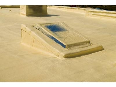 Poddasze z oknem dachowym pokryte jednolitą warstwą jasnej pianki izolacyjnej, widoczne elementy konstrukcyjne i komin również zabezpieczone pianką.