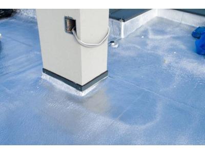 Błyszcząca, srebrzysta izolacja natryskowa na płaskim dachu wokół pionowego komina z wystającym kablem elektrycznym.