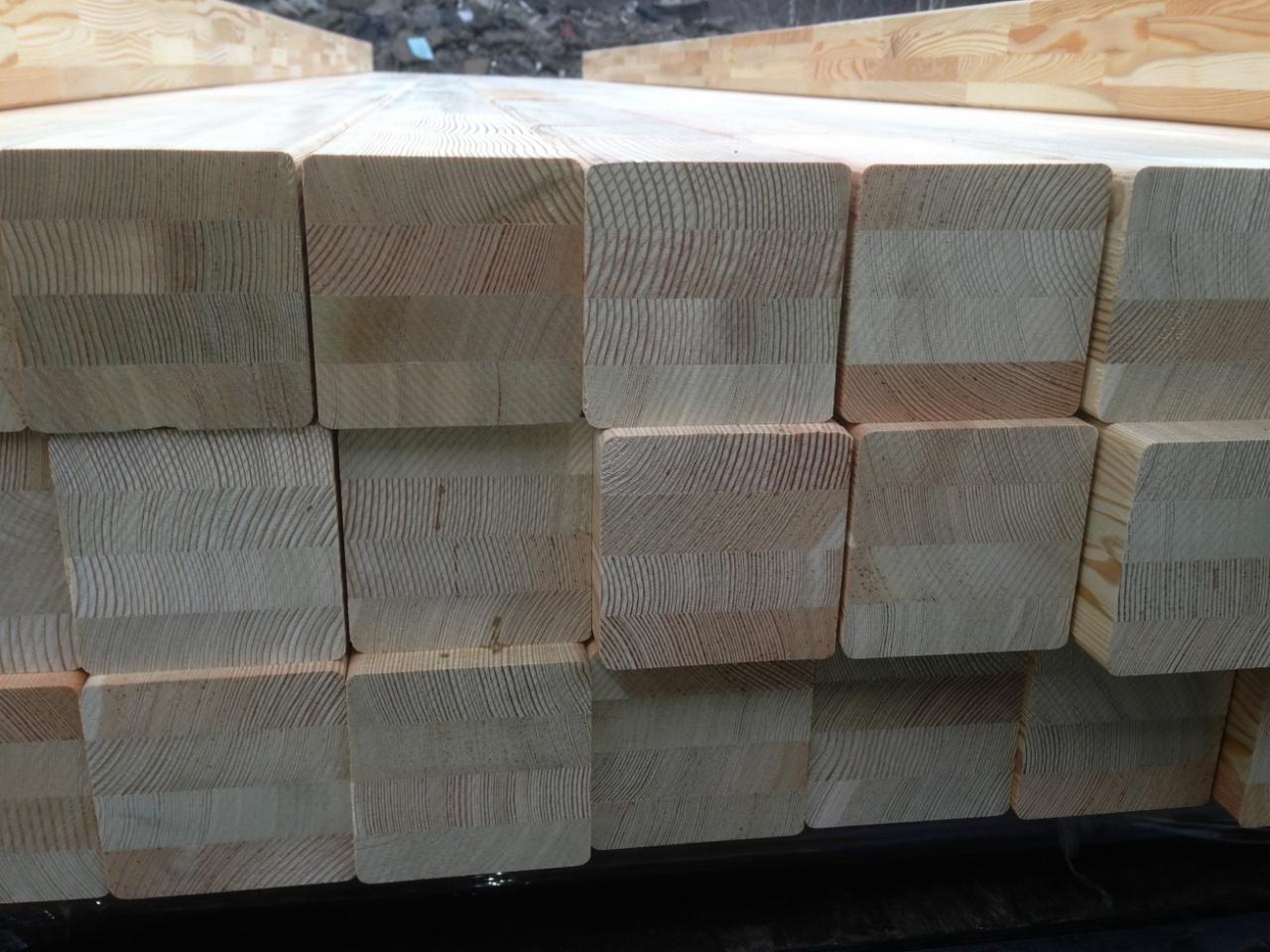 Stos kantówki klejonej warstwowo, widoczne słoje drewna i warstwy klejenia, przygotowane do transportu.