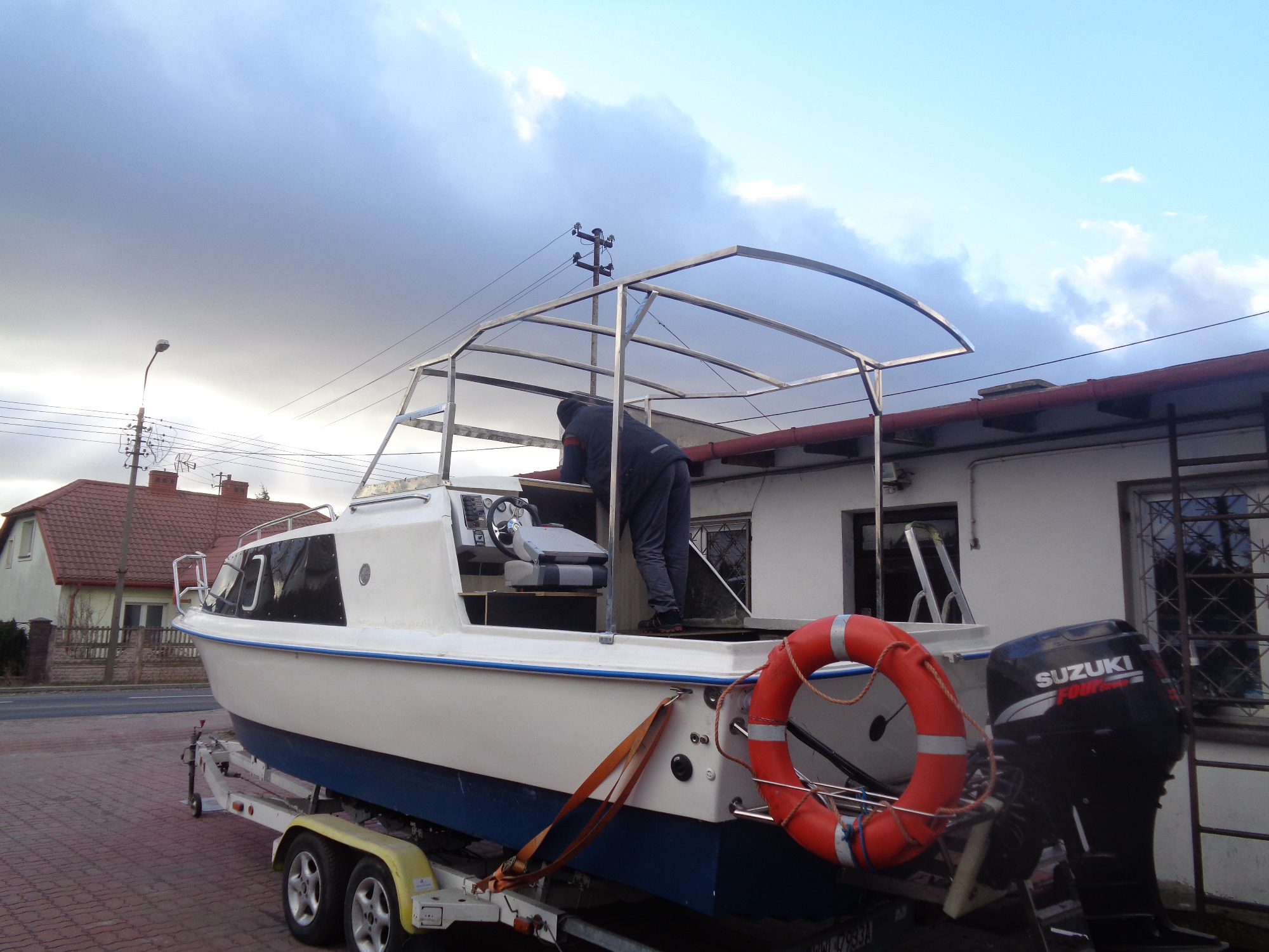 Konstrukcja metalowa nadbudowy łodzi w trakcie montażu, widoczny pracownik wewnątrz kabiny, łódź na przyczepie z silnikiem Suzuki.