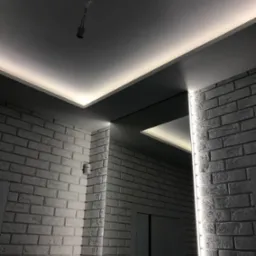 Nowoczesne oświetlenie LED w suficie podwieszanym z szarą wnęką, biała cegła na ścianach, widoczna oprawka żarówki na kablu.