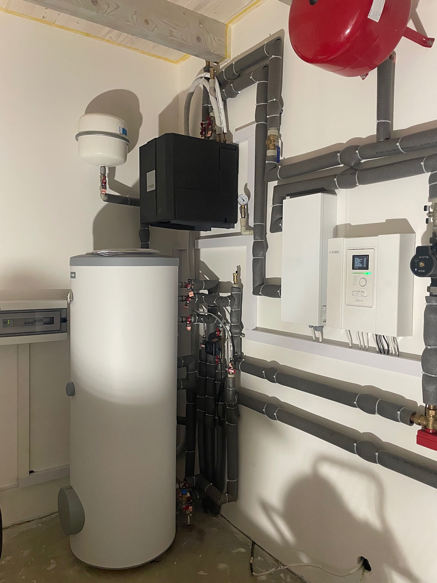 Złożona instalacja grzewcza Nibe: pompa ciepła, zbiornik buforowy i rozbudowany system rur z izolacją termiczną w schludnym pomieszczeniu technicznym.