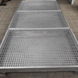 Trzy metalowe, kwadratowe kraty podłogowe z niskoprofilowymi nóżkami, ułożone jedna za drugą na szarej posadzce w hali.