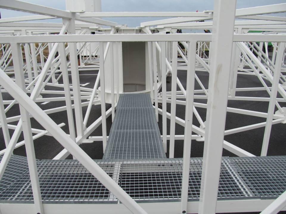 Wnętrze konstrukcji stalowej hali z pomostem z kraty pomostowej, widok z góry na czarny asfalt.